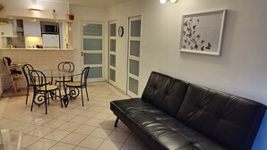 Ein kompakter Wohnbereich mit Essplatz, einem schwarzen Ledersofa, einer Küche mit Mikrowelle und einer Uhr an der Wand.