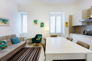 A modern living room with a sofa, a dining table, and a kitchen area. - Downtown, serene nights overlooking quiet garden, GARDEN HOUSE (Napoli)