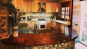 A kitchen with wooden cabinets, a stone wall, and a wooden countertop. - Remote mountain villa with stunning views and private pool to sleep up to six (Los Cerricos)