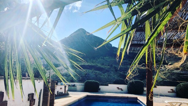 A pool area with a mountain in the background, surrounded by palm trees and a white wall with decorative elements. - Remote mountain villa with stunning views and private pool to sleep up to six (Los Cerricos)