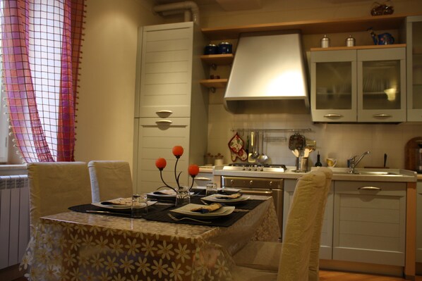 A dining area with a table set for four, a kitchen with white cabinets, and a window with a red curtain.