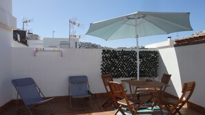A patio with a table and chairs, a blue umbrella, and a green wall.