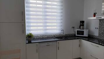 Een moderne keuken met raam, witte kastjes, een magnetron en een koffiezetapparaat.