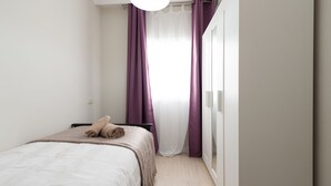 A minimalist bedroom with a bed, a wardrobe, and a window with purple curtains.