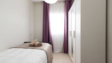 Een minimalistische slaapkamer met een bed, een garderobe en een raam met paarse gordijnen.
