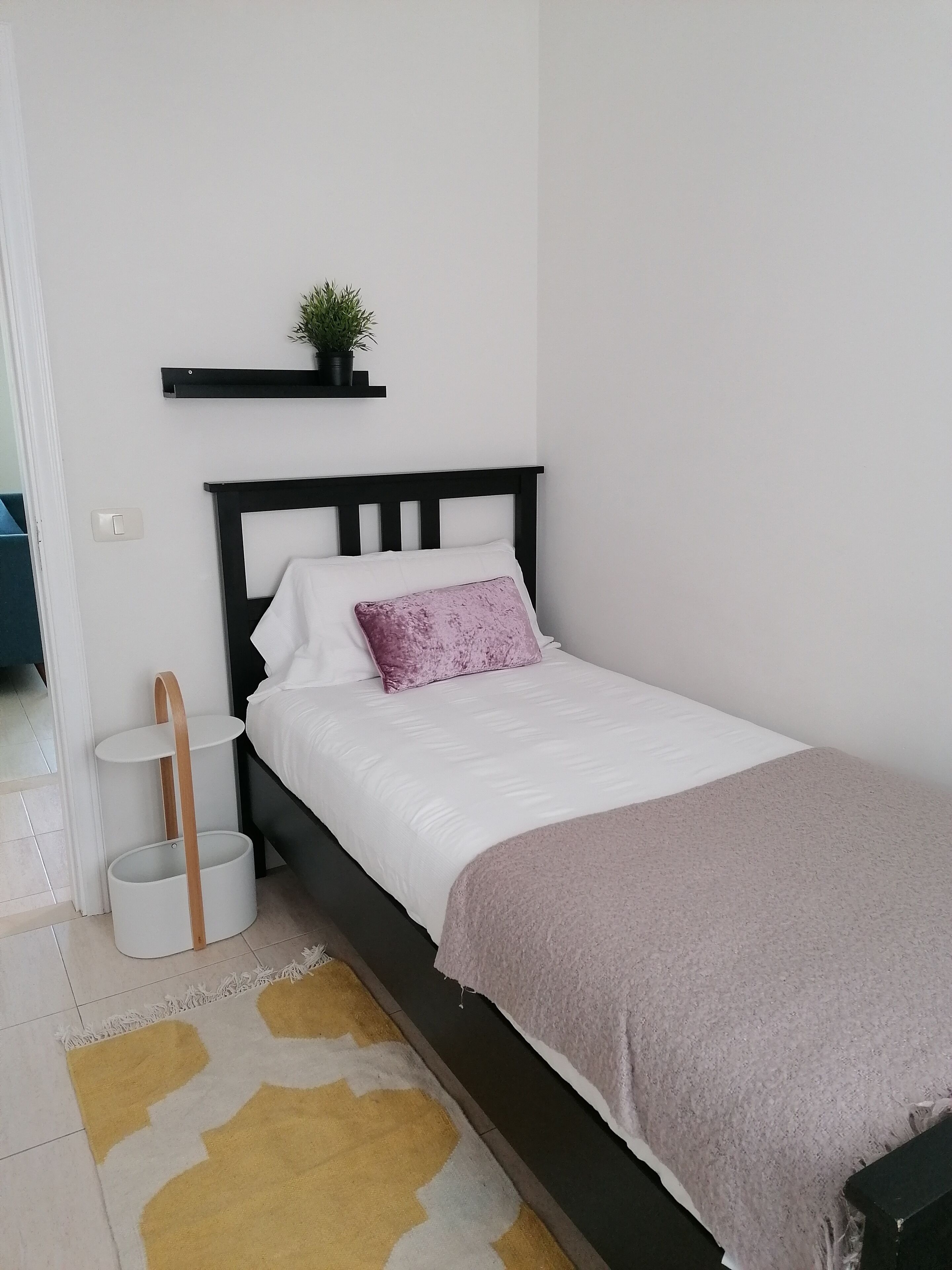Ein Schlafzimmer mit Bett, Nachttisch, Wandregal und einer kleinen Topfpflanze.
