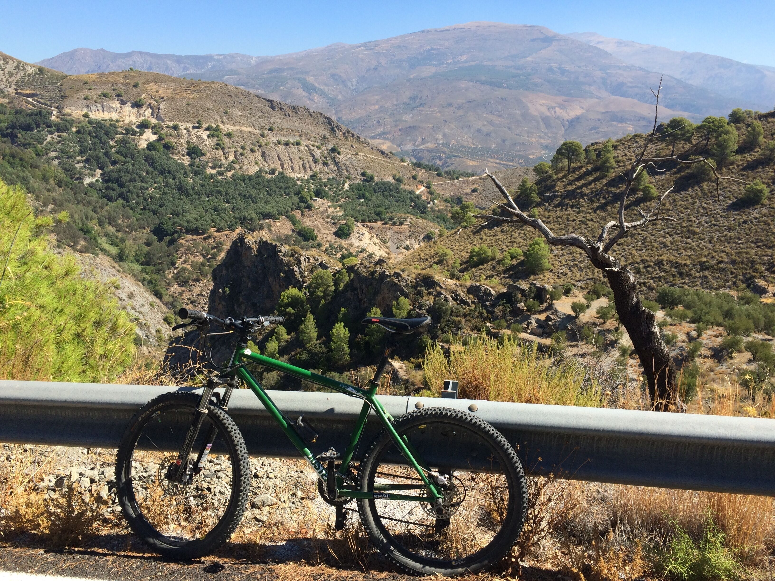 Una bicicleta de muntanya aparcada al costat d'una barana amb vista a un paisatge montanyós.