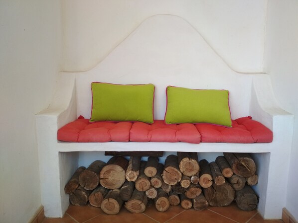 A white bench with red cushions and green pillows, placed under a white wall with a curved top.