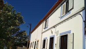 Una calle estrecha con un edificio blanco y detalles amarillos, y un techo de tejas rojas.