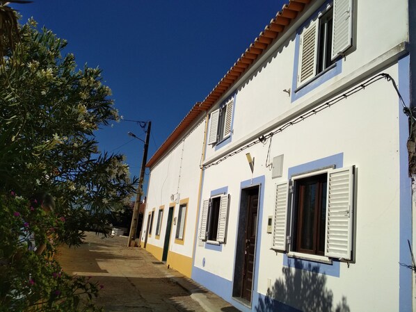 A narrow street with a white building with yellow trim and a red-tiled roof.