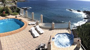 A pool area with a hot tub and lounge chairs, overlooking the ocean.