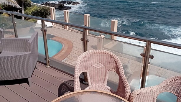 A balcony with wicker furniture overlooking a pool and the ocean.