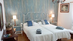 A double bed with white and blue striped bedding, a small bedside table with a lamp, and a wall-mounted chandelier.