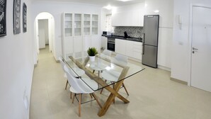 Una cucina moderna con mobili bianchi, un frigorifero in acciaio inossidabile e un tavolo da pranzo con piano in vetro e gambe in legno.