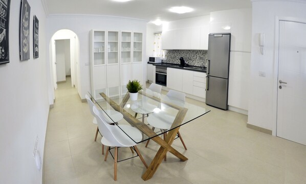 A modern kitchen with white cabinets, a stainless steel refrigerator, and a glass-top dining table with wooden legs. - Modern and new downtown apartment in Puerto de la Cruz (Puerto de la Cruz)