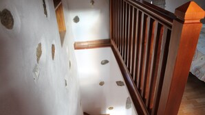 Una scala in legno con corrimano, pareti bianche con dettagli in pietra e un tappeto decorato alla base.