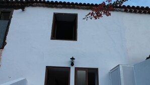 Un edificio bianco con due finestre, una aperta, e un piccolo fiorale sopra la porta.