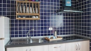 Una cucina con zoccolo paraschizzi blu, lavello in acciaio inossidabile, ripiano in legno con stoviglie e cappa aspirante blu.