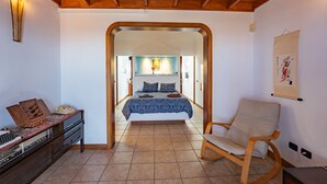 Ein Schlafzimmer mit Holzboden, einem Bett mit blauer Bettdecke, einem Sessel und einem Schreibtisch mit Telefon und Radio.