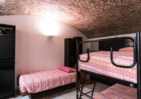 A dormitory room with bunk beds, a single bed, a wardrobe, and a wall-mounted light fixture.