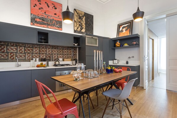 A modern kitchen with a wooden table, red and gray chairs, and a built-in oven.