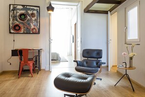 A modern living room with a black leather sofa, a red chair, a desk, and a painting on the wall.