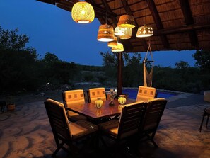 An outdoor dining area with a table and chairs, surrounded by hanging lanterns, under a thatched roof. - Bushvilla Umoja Kruger - wildlife without fences (Phalaborwa)