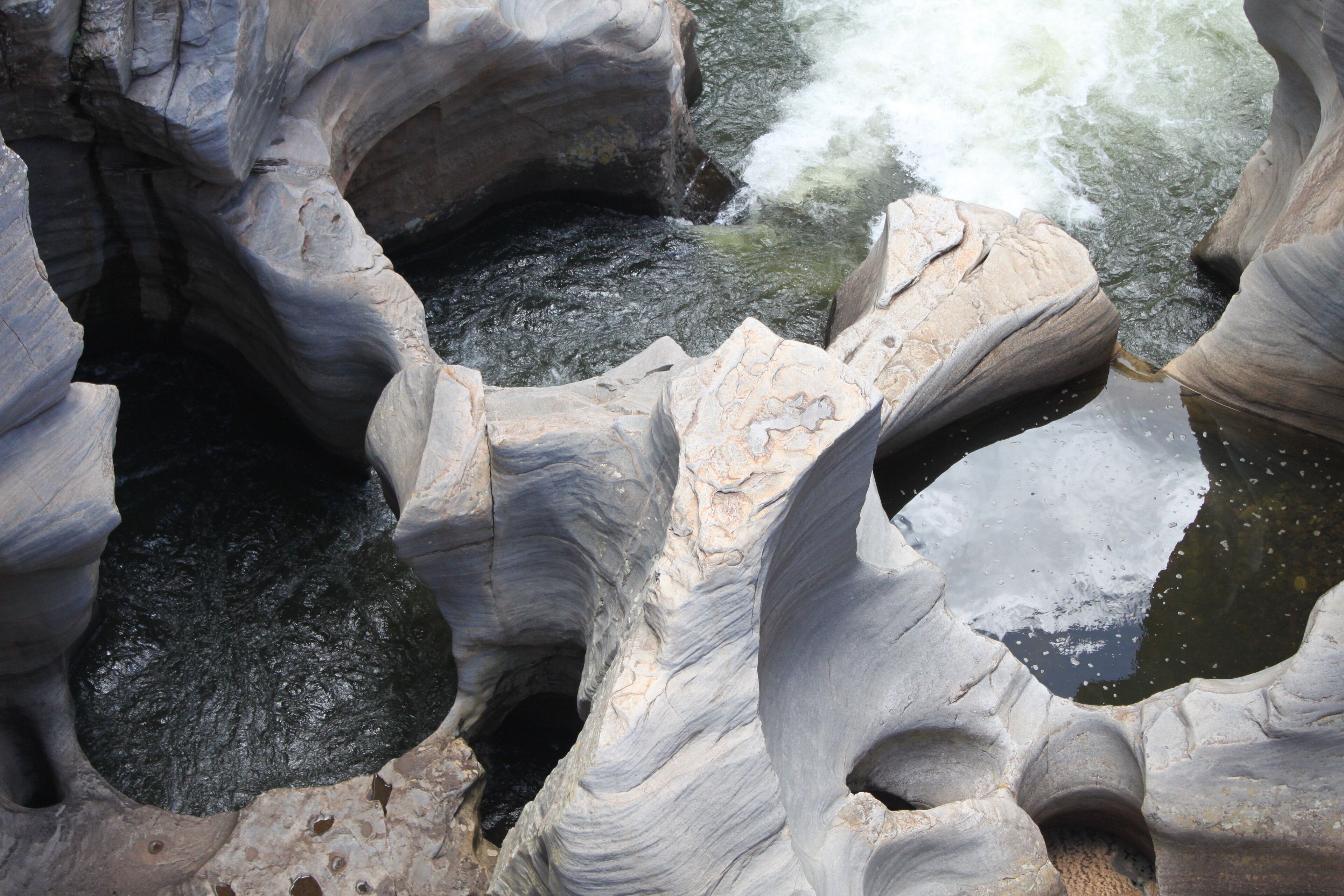 A natural rock formation with a narrow passageway and a water stream flowing through it.