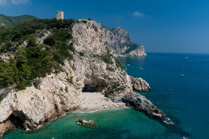 A coastal landscape with a rocky beach, clear turquoise waters, and a tower on a hill.