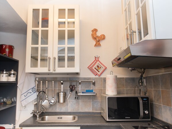 A kitchen with a stainless steel sink, a microwave, and a cabinet with glass doors.