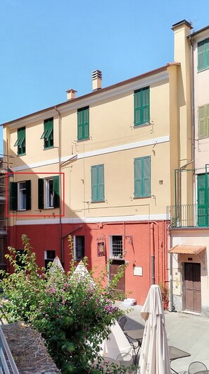 A multi-story building with green shutters, a red lower floor, and a beige upper floor.