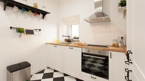 A modern kitchen with white cabinets, a black and white checkered floor, a stainless steel range hood, and a wooden countertop.