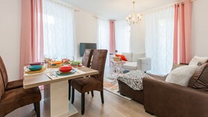 A modern living room with a dining area, featuring a sofa, chairs, a table set with dishes, and a TV.