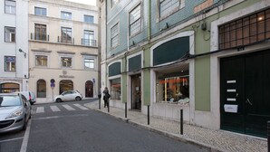 A street view with a building featuring a shop with glass display windows and a closed door.
