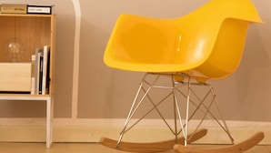 Une pièce avec un plancher en bois, une bibliothèque blanche et un fauteuil à bascule jaune.