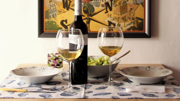 Une affiche encadrée représentant un toucan tenant un verre de bière Guinness, avec une bouteille et des verres de vin posés sur une table.