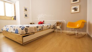 Une chambre à coucher avec un lit, un fauteuil à bascule, une petite table et des tableaux encadrés accrochés au mur.