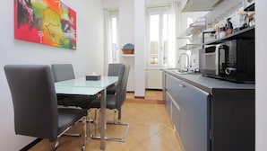Une cuisine moderne avec un coin repas, comprenant une table en verre, des chaises noires et un tableau abstrait aux couleurs vives accroché au mur.