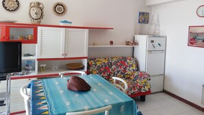 A compact kitchen with a refrigerator, microwave, and a dining table with a patterned tablecloth. - A WINDOW ON THE SEA (Roccalumera (ME))
