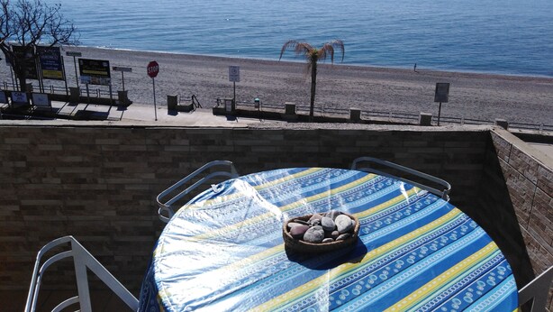 A beachside view with a table covered in a patterned tablecloth, a bowl of stones, and a stop sign in the background. - A WINDOW ON THE SEA (Roccalumera (ME))