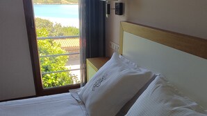 Ein Hotelzimmer mit Bett, Nachttisch, Lampe und Blick auf Wasser und Grünflächen.