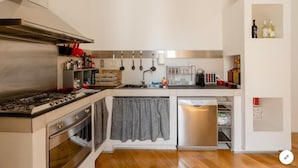 A compact kitchen with a gas stove, oven, and dishwasher, a hanging rack for utensils, and a small wine fridge. - Bijoux Luxury Apartment in Old Town (Bari)