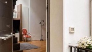 A modern interior with a staircase leading to a second floor, a red chair, and a small table with flowers. - Bijoux Luxury Apartment in Old Town (Bari)