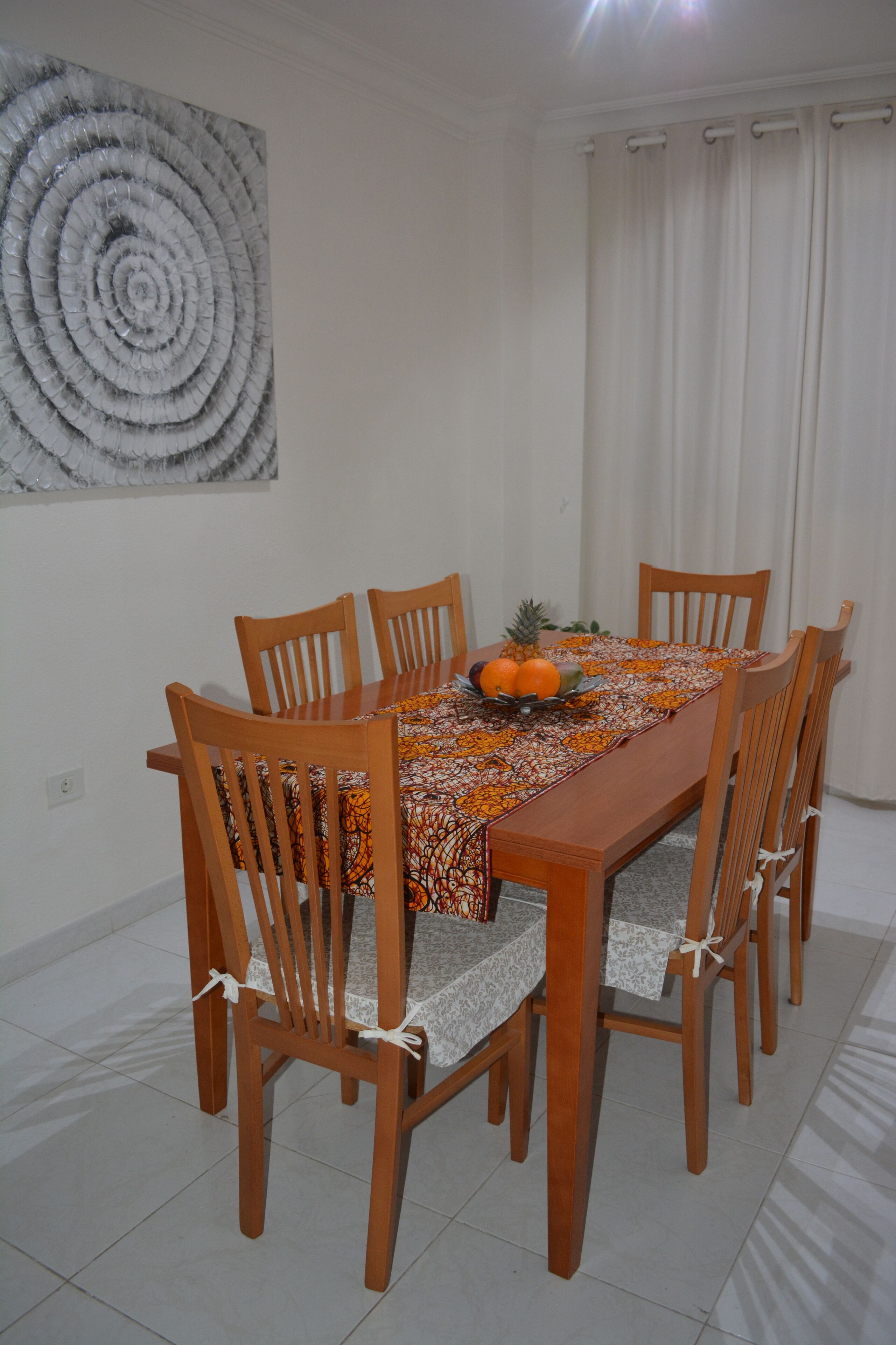 Un comedor con una mesa y sillas de madera, un frutero y un mantel estampado.