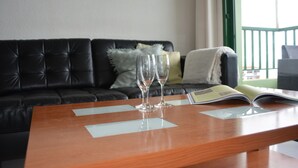 Uma mesa de madeira com dois copos de vinho vazios e uma revista, em frente a um sofá de couro preto com um corrimão verde ao fundo.