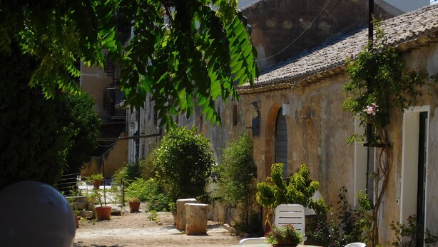 A courtyard with a table and chairs, surrounded by potted plants and a building with a tiled roof. - Comfortable apartment for exclusive use (Valderice)