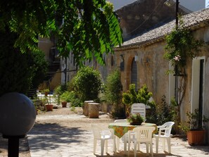 A courtyard with a table and chairs, surrounded by potted plants and a building with a tiled roof.