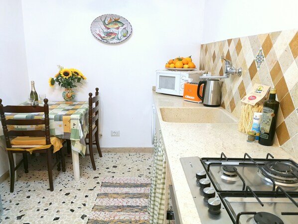 A compact kitchen with a gas stove, a microwave, and a sink. There is a dining table with chairs and a vase of sunflowers.