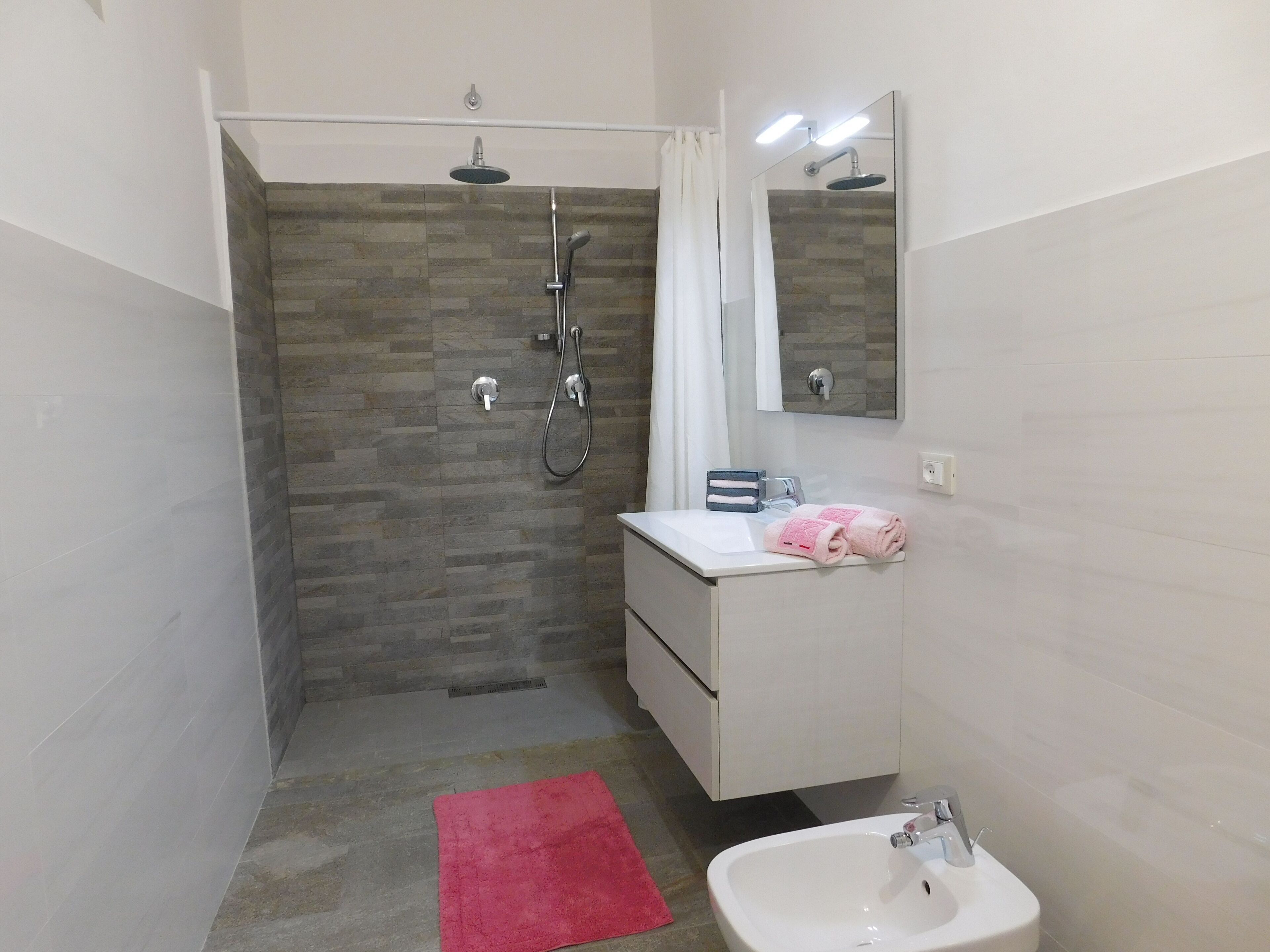 Ein modernes Badezimmer mit Dusche, Waschbecken und Spiegel.