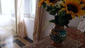 A room with a tiled floor, a window with curtains, and a table with a vase of sunflowers. - Comfortable apartment for exclusive use (Valderice)